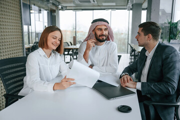 Working with a plan. Muslim businessman in traditional outfit with colleagues in office