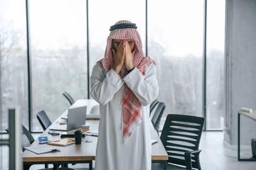 Praying with hands near the face. Successful Muslim businessman in traditional outfit in his office