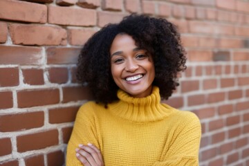 Curly African American woman wearing yellow shirt against red brick wall background