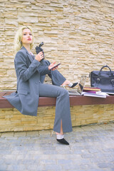 portrait of a businesswoman in a business suit with a phone in her hands. a woman is sitting on a bench with a laptop, notepads and a bag are layout next to her.