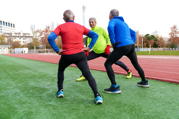 Back view of senior runners doing back stretches on a track, taking a restful break during their workout
