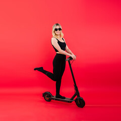 Fototapeta na wymiar Female in sport clothes stands on electric scooter with sunglasses on red and white background