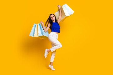 Fototapeta na wymiar Full length photo of cheerful excited lady dressed blue top rising shoppers empty space isolated yellow color background