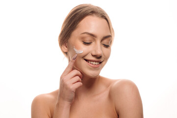 Beauty portrait of a beautiful woman applying cream on her face on an isolated white background. Skin care concept