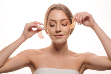 Beauty portrait of a beautiful woman applying gel eye patches on her face on a white background