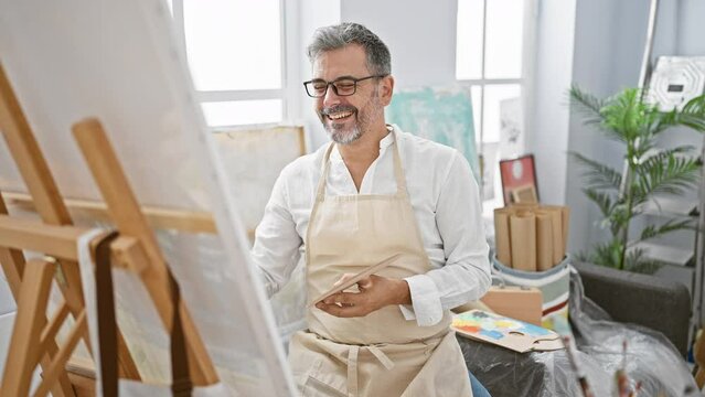 Confident, smiling young hispanic man with grey hair joyfully drawing his masterpiece in a cozy art studio