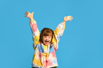Careless and caring childhood. Happy smiling girl, child with down syndrome against blue studio...