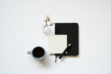 Workspace. black notebook, memopad, cup of coffee, pencil, dry plant on white desk background. flat lay, top view