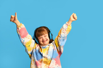 Happy smiling teen girl with down syndrome listening to music in headphones, expressing joy against...