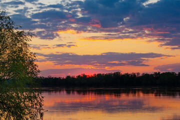Sunset landscape with clouds over a wide river in the countryside on a summer evening
