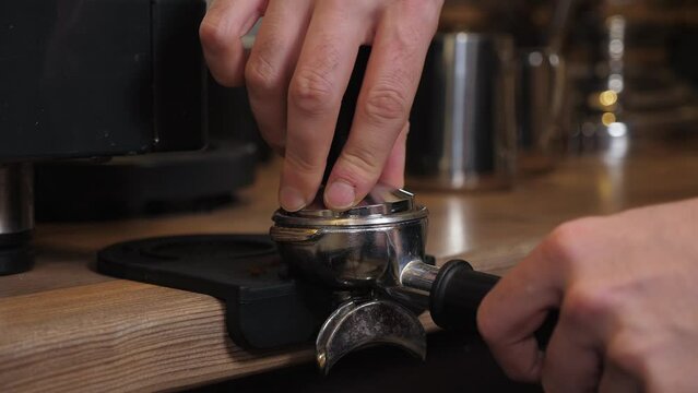 Close-up of a barista tempering freshly ground coffee with a tempera in a coffee shop. The process of making espresso.
