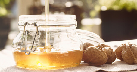 Organic liquid honey in a glass jar next to whole walnuts - 707864585
