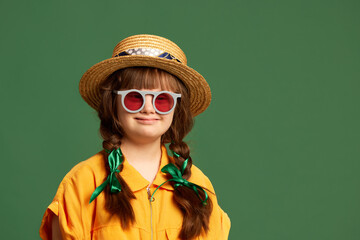 Portrait of beautiful little girl with down syndrome wearing hat, sunglasses and yellow suit...