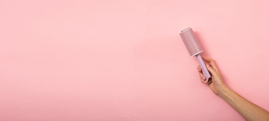 Lint roller in a woman's hand on a pink background.