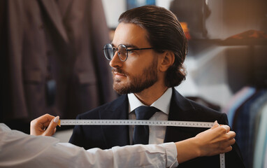 Banner Atelier Classic Menswear. Woman tailor taking measurements of young handsome man, fitting bespoke suit to model