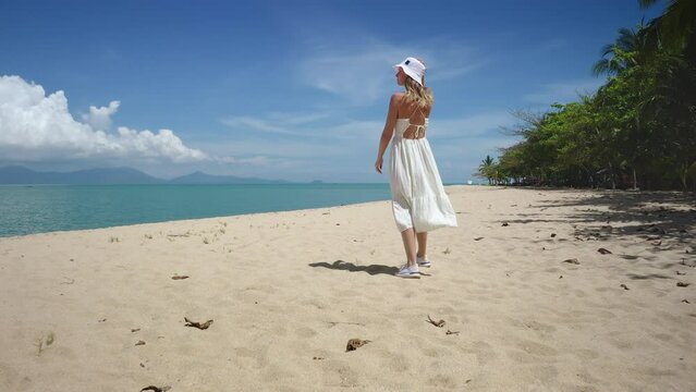 Female in white dress walking tropic sand beach. Palm trees, blue sky, crystal water, sunny day. Exotic island travel, outdoor lifestyle, summer holiday vacation, relax, enjoy nature of Thailand
