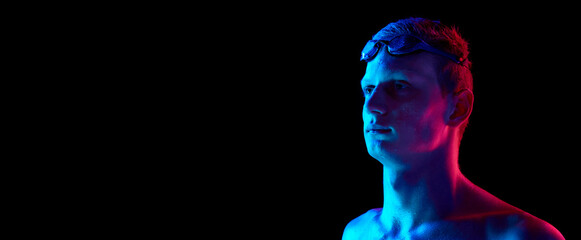 Portrait of serious, concentrated young man with goggles, swimmer posing against black studio background in neon light. Power, endurance. Poster for ad. Promotion of sport events