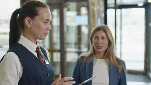Female hostess using digital tablet and greeting just arrived guests in hotel lobby