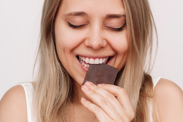 Cropped shot of a young caucasian cheerful blonde woman eating dark bitter chocolate on a white background. Close up