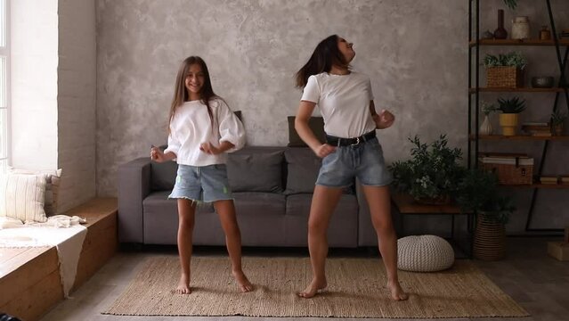 Mother and daughter teenager having fun dancing in living room. Parenting concept.