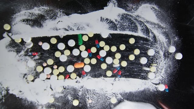 Hand scatters pills on a table covered with cocaine white powder mess on the table after a party drugs and pills lie on the table