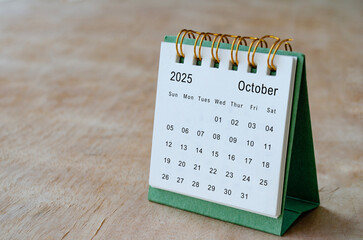 October 2025 table calendar on wooden desk with customizable space for text. Copy space and...