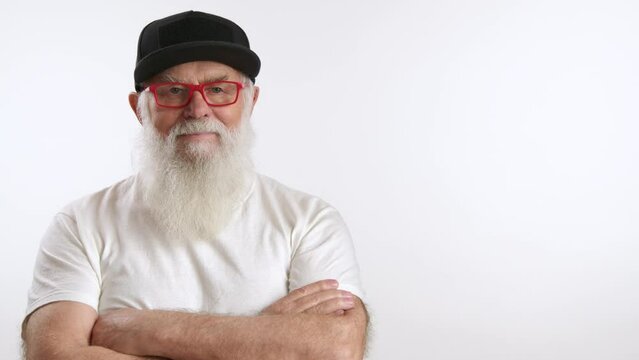 A youthful senior man confidently crosses his arms over his chest, exuding strength and determination. Dressed in a youthful style, he sports a black cap, red glasses, and a white t-shirt. 8K RAW.