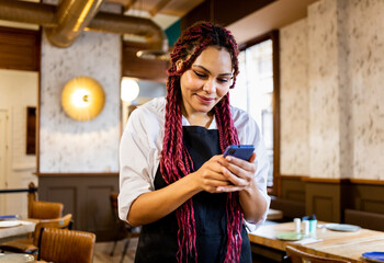 A dark-skinned woman dressed as a waitress is working inside a cafe. The girl is taking notes with...