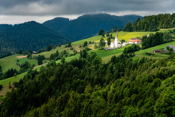 Landscape of Slovenia. A small church in the middle of the fields behind a forest - 707950902