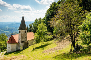 Landscape of Slovenia. A small white church is nestled in the mountain between meadow and forest - 707951125