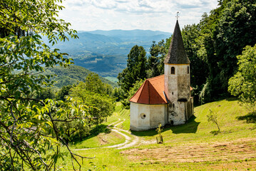 Landscape of Slovenia. A small white church is nestled in the mountain between meadow and forest - 707951143