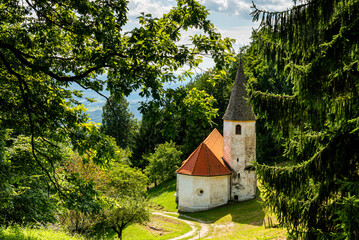 Landscape of Slovenia. A small white church is nestled in the mountain between meadow and forest - 707951170