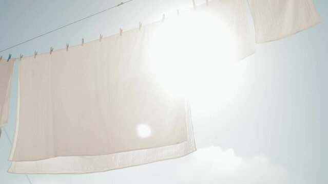Slow motion. White, washed bed linen against a blue, sunny sky. The wind sways white linen against the backdrop of a bright sky. Washing, cleanliness, home, household, cleaning, housekeeping, fresh