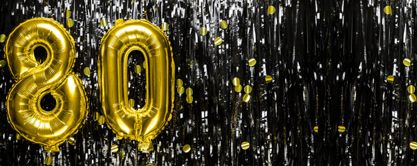 Gold foil balloon number number 80 on a background of black tinsel decoration. Birthday greeting...