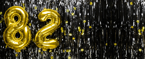 Gold foil balloon number number 82 on a background of black tinsel decoration. Birthday greeting...