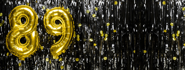 Gold foil balloon number number 89 on a background of black tinsel decoration. Birthday greeting...