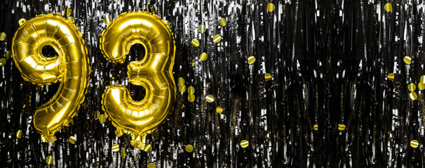 Gold foil balloon number number 93 on a background of black tinsel decoration. Birthday greeting...
