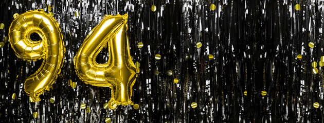 Gold foil balloon number number 94 on a background of black tinsel decoration. Birthday greeting...