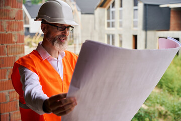 Pleased contractor analyzing architectural drawings on building site