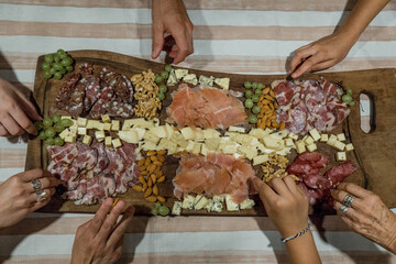 Hands grabbing food from a delicatessen board with cold meats, cheeses, nuts and grapes. Sharing...