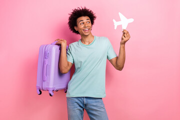 Photo of cool excited guy wear blue t-shirt rising baggage holding paper plane empty space isolated...