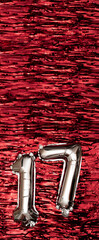 Silver foil balloon number number 17 on a background of red tinsel decoration. Birthday greeting...
