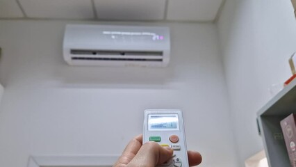 Closeup man hand holding a remote control to the air conditioning system pressing buttons as try to adjust the temperature in the room to a comfortable level. Home heating during cool season