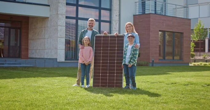 Happy family looking at camera with solar panel. Parents and children smiling at lawn at background of modern house. Mother and father instilling in kids love of planet. Eco awareness concept.