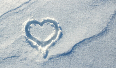 Top view, hand-drawn a heart on natural pure white soft snow surface. Symbol of love in winter...