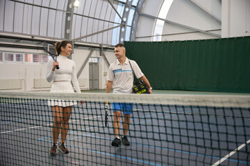 Woman with man instructor after playing tennis game at indoor court