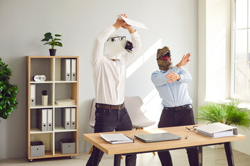 Half animal half people having fun at end of work week. Male corporate workers in horse and dinosaur masks having party. Funny happy men with weird horse and T rex dino faces dancing by desk in office