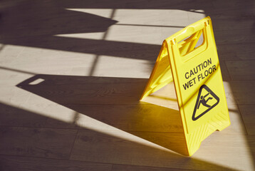 Yellow warning sign on the floor alerts to potential hazards, cautioning about a wet surface. An...