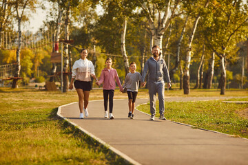 Sporty happy family with children wearing sportswear holding hands walking together in the park after sport workout outdoors. Healthy lifestyle, training and fitness in nature concept.