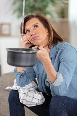 worried mature woman collecting water leakage from ceiling